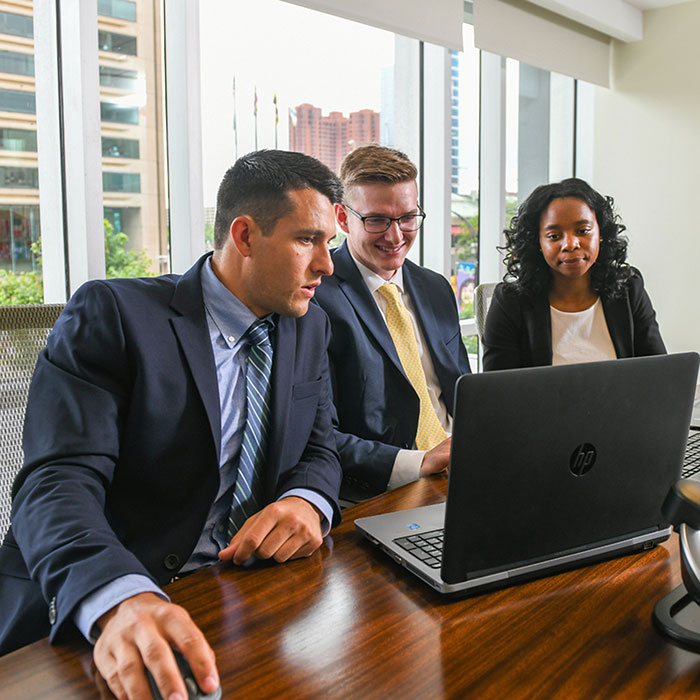 Three students working at a latptop at their internship in downtown baltimore