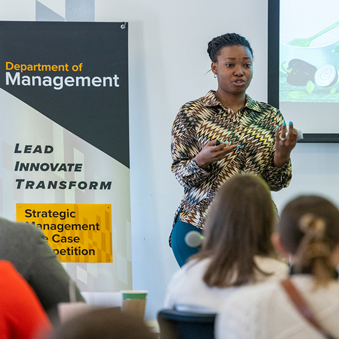 student presents in front ofa group of people at a Department of Management case competition