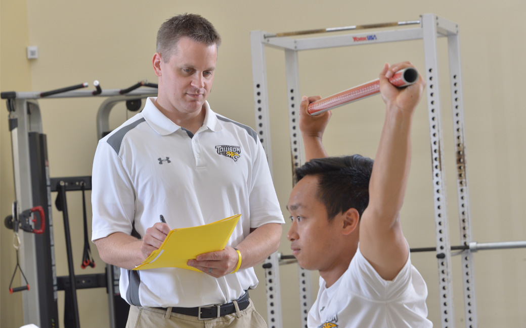 Professor Peter Lisman with a student lifting a bar