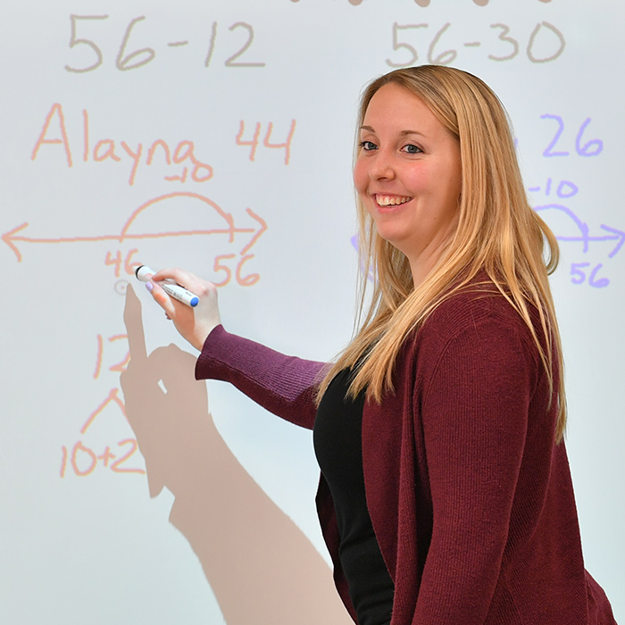 Professor at white board writing.
