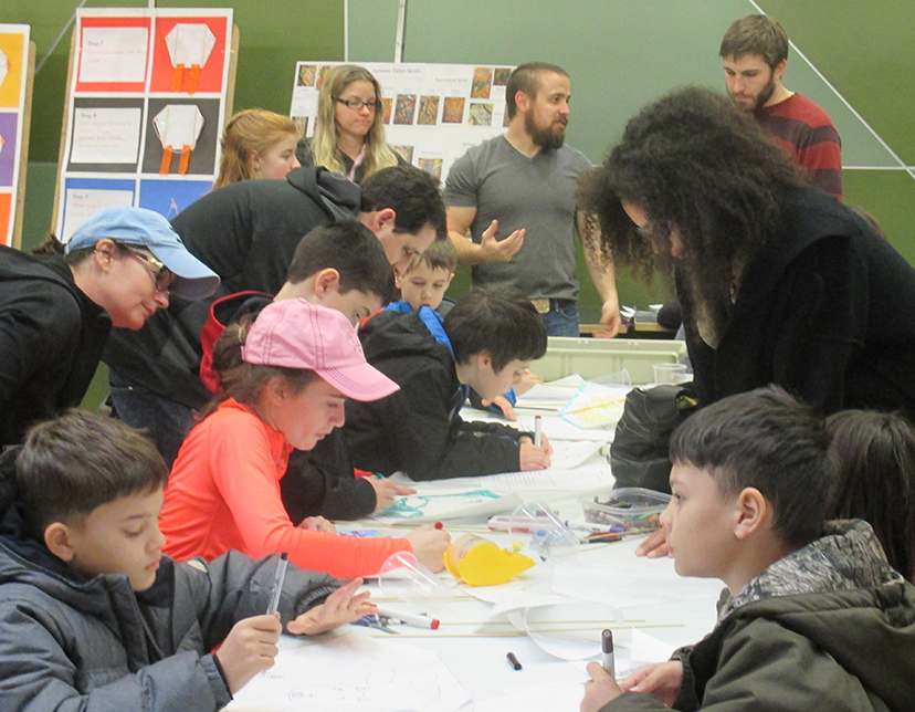 Families sit at a table working on art