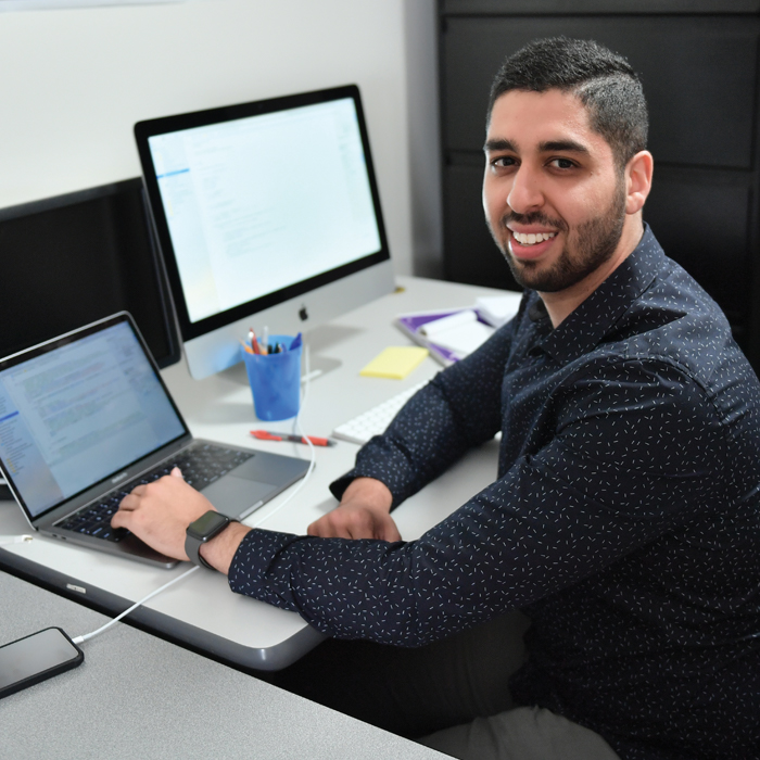 Jal Irani in front of a computer, smiling at the camera