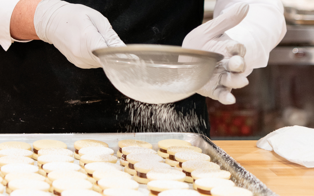 Woman's hands shaking sugar over baked goods through a sieve