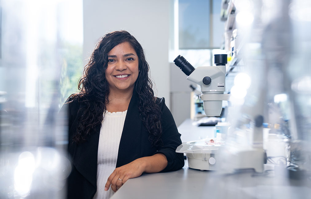 Woman leans on lab station with microscope