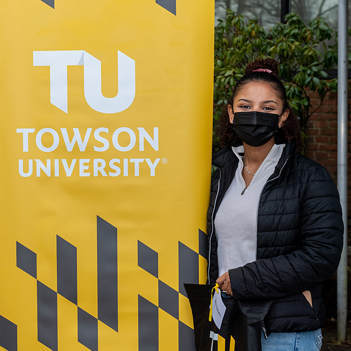 Masked student standing next to TU banner