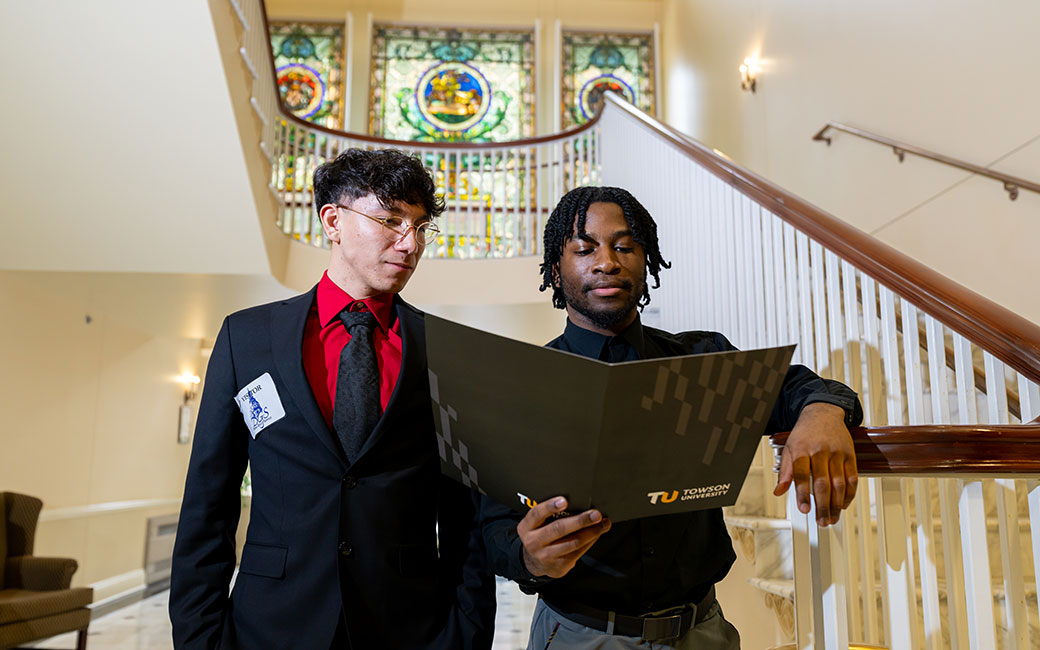 Two students standing and reading from a branded TU folder