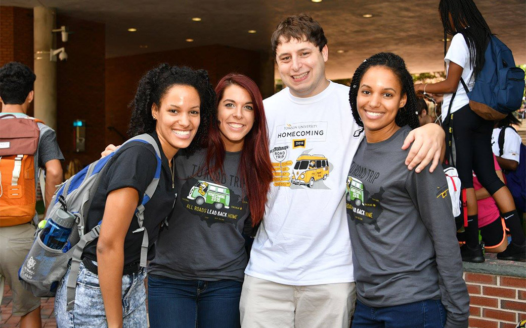 A group of four students hugging, standing together, in front of lecture hall